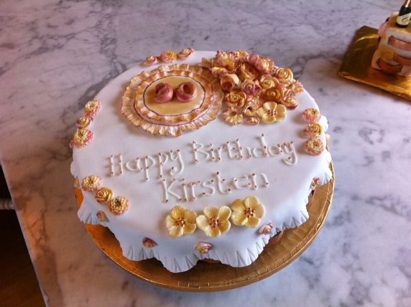 gold flowers on a white circular birthday cake with the text 'Happy Birthday Kirsten'