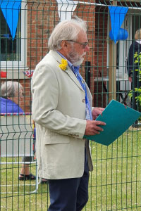 A man in a cream blazer and blue shirt with a yellow flower 