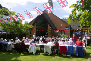 A long table outside filled with people, above them is union jack bunting