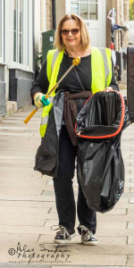 a woman holding a bin bag walking down the street