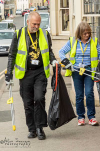 Two people wearing high vis jackets walking along a street and picking up rubbish