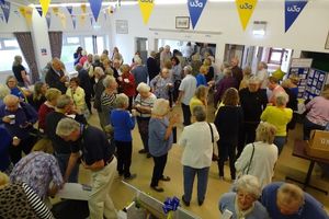 A busy hall full of people. There is blue and yellow u3a bunting hanging from the ceiling.