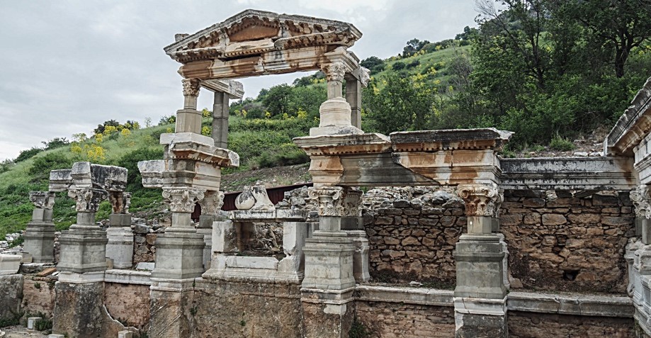 a photo of crumbling roman ruins of a building, with a grassy hill behind