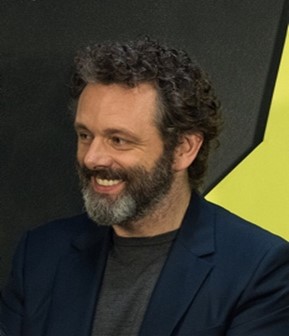 man with black hair and greying beard smiling in navy suit blazer