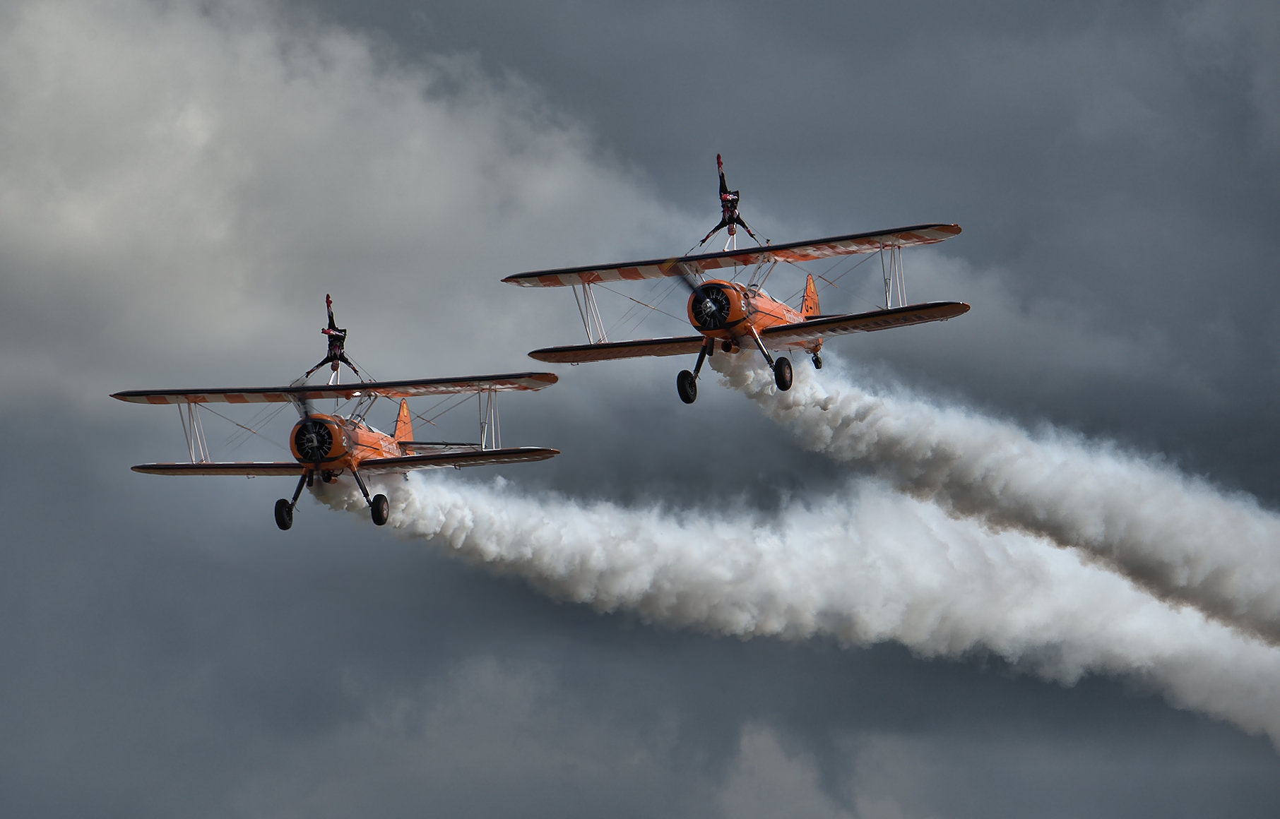 two people on top of planes with trail in sky