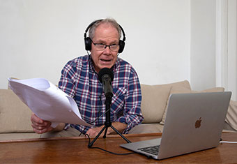 A u3a Radio Podcast host reads from a sheet of paper into a microphone connected to a laptop