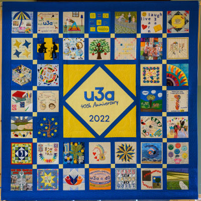 A colourful quilt with forty squares and in the middle a big yellow diamond reading u3a 40 anniversary 