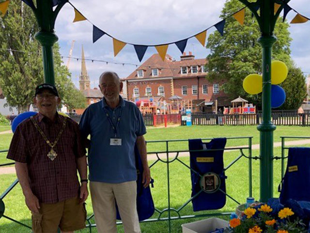 a man and a mayor standing in ab and stand with blue and yellow bunting and balloons