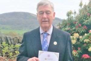 A man standing outside holding a certificate that says 'Coronation Champion Harry Roy Biggs'