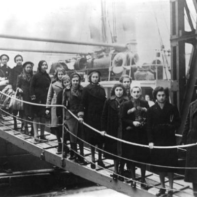 a black and white photo of about 20 girls and women waiting in a queue to come off a boat