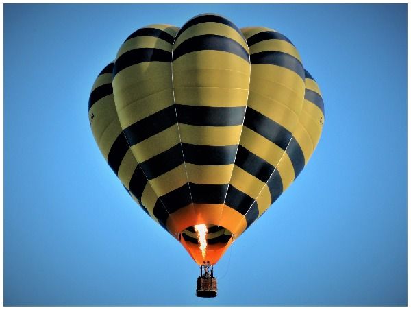 A yellow and black striped hot air balloon, in flight on a clear day