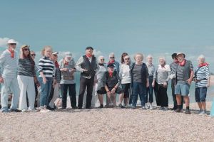 A group of people, all wearing stripy tops, standing on a beach, singing