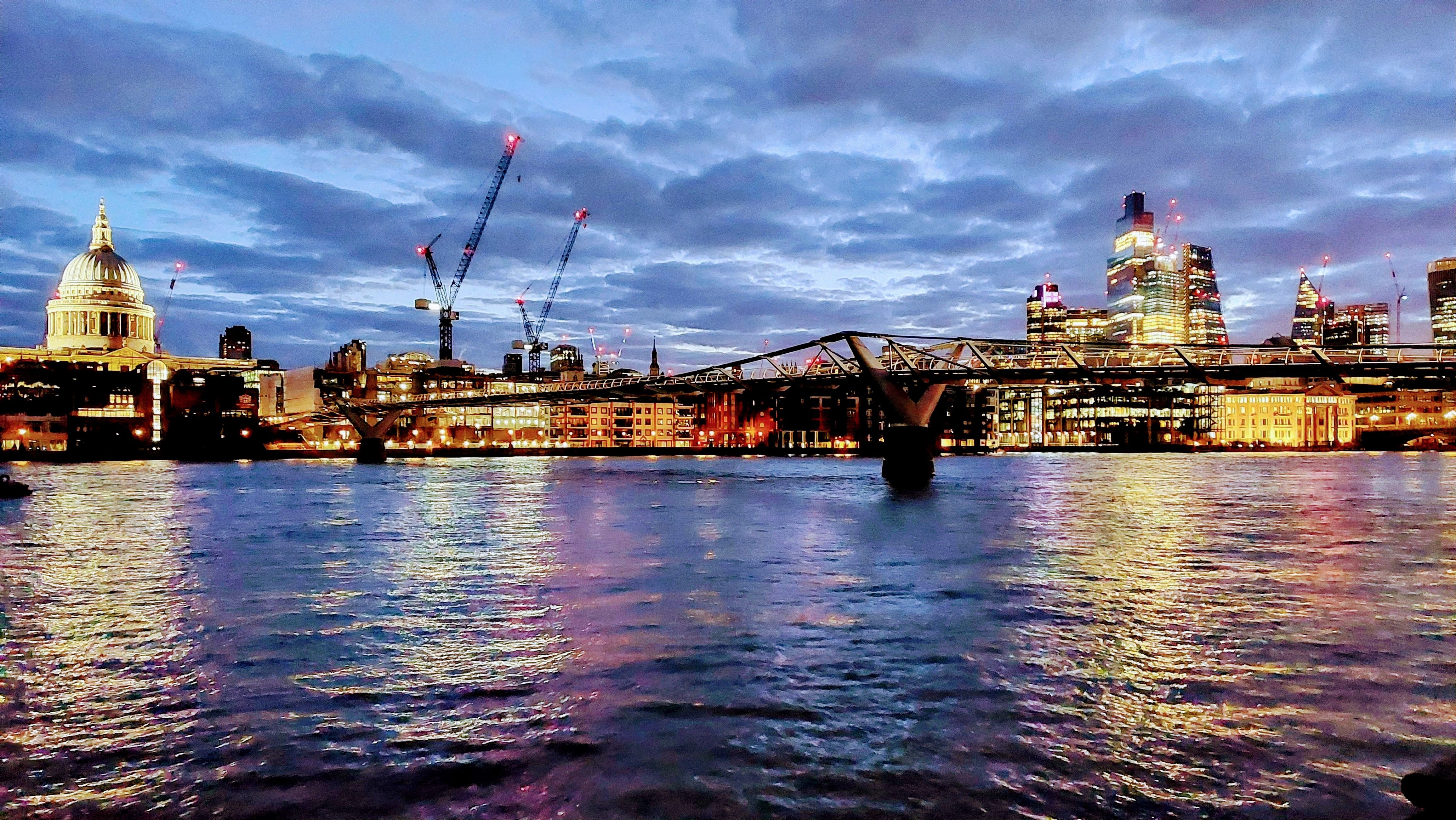 London at 6am, river in front and buildings in the background. It's getting light and the buildings are lit up with yellow lights. 