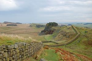 a cloudy sky and green fields, with hadrian's wall running across the fields