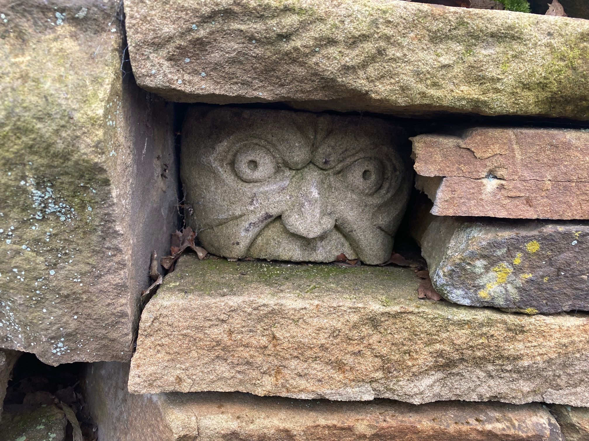part of a stone head sculpted like a face, in between bricks of a wall