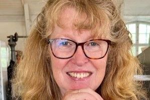 a woman with dark blonde curly hair and glasses smiling