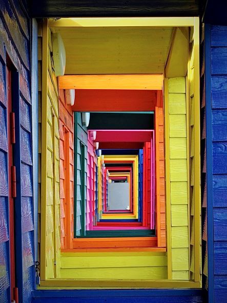 brightly coloured wooden beach huts viewed through a gap in the side 