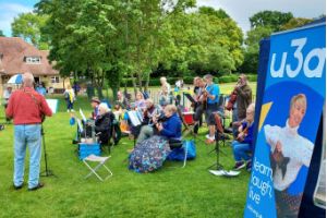 Musicians of Hillingdon u3a in a park next to a u3a flag banner