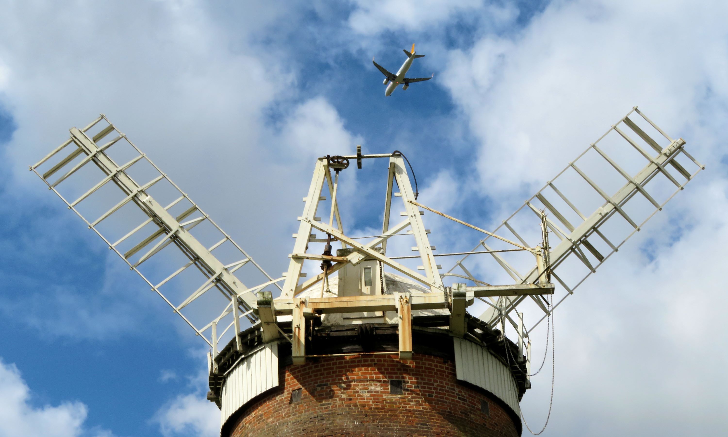 looking up at a windmill with a plane flying overhead